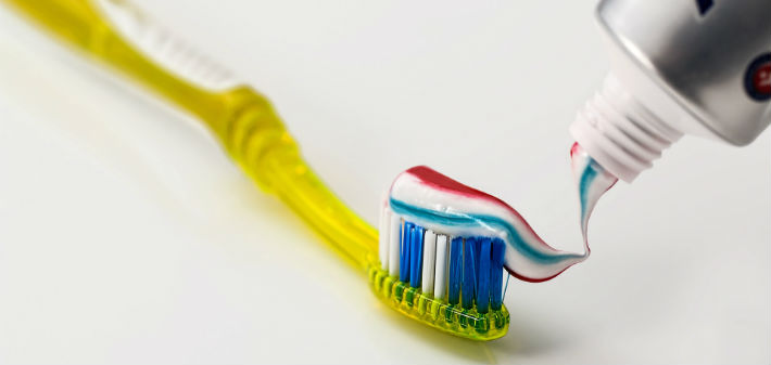A transparent yellow toothbrush is spread with red, white, and blue toothpaste from a tube.