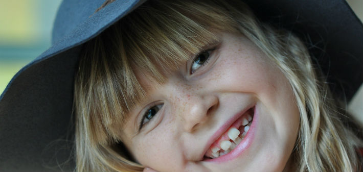 A little girl in a big hat smiles with widely spaced teeth.