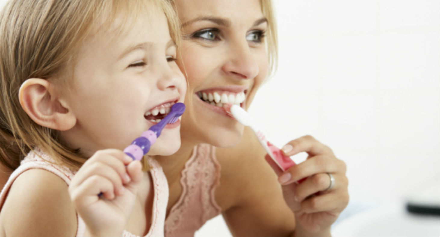 A mother and her toddler daughter practice dental care for children together.