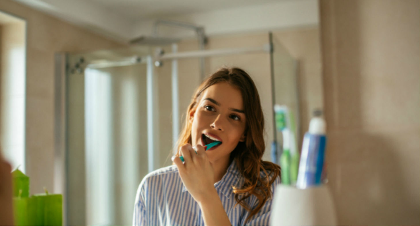 A young woman brushes her teeth in her bathroom, focusing on her dental hygiene.