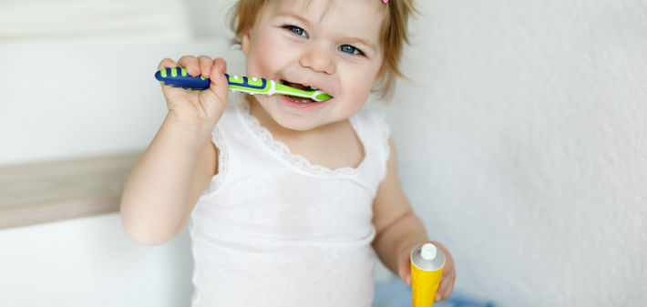 A toddler girl practices dental care for children by brushing her teeth happily.