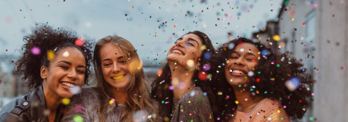 Four beautiful women celebrate with confetti and smile, displaying their perfectly, professionally whitened teeth.