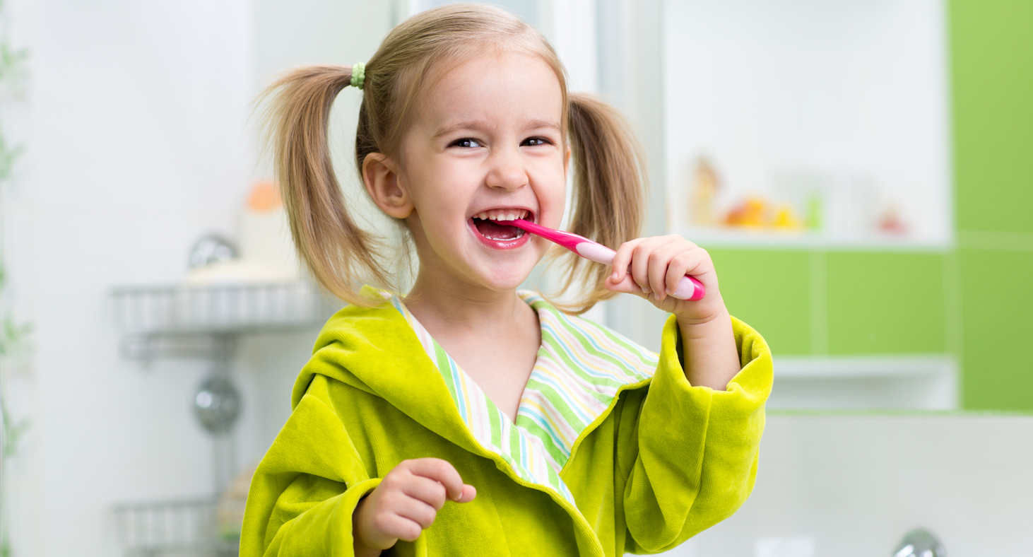 A little girl with pigtails brushes her teeth, practicing what her children's dentist has shown her.