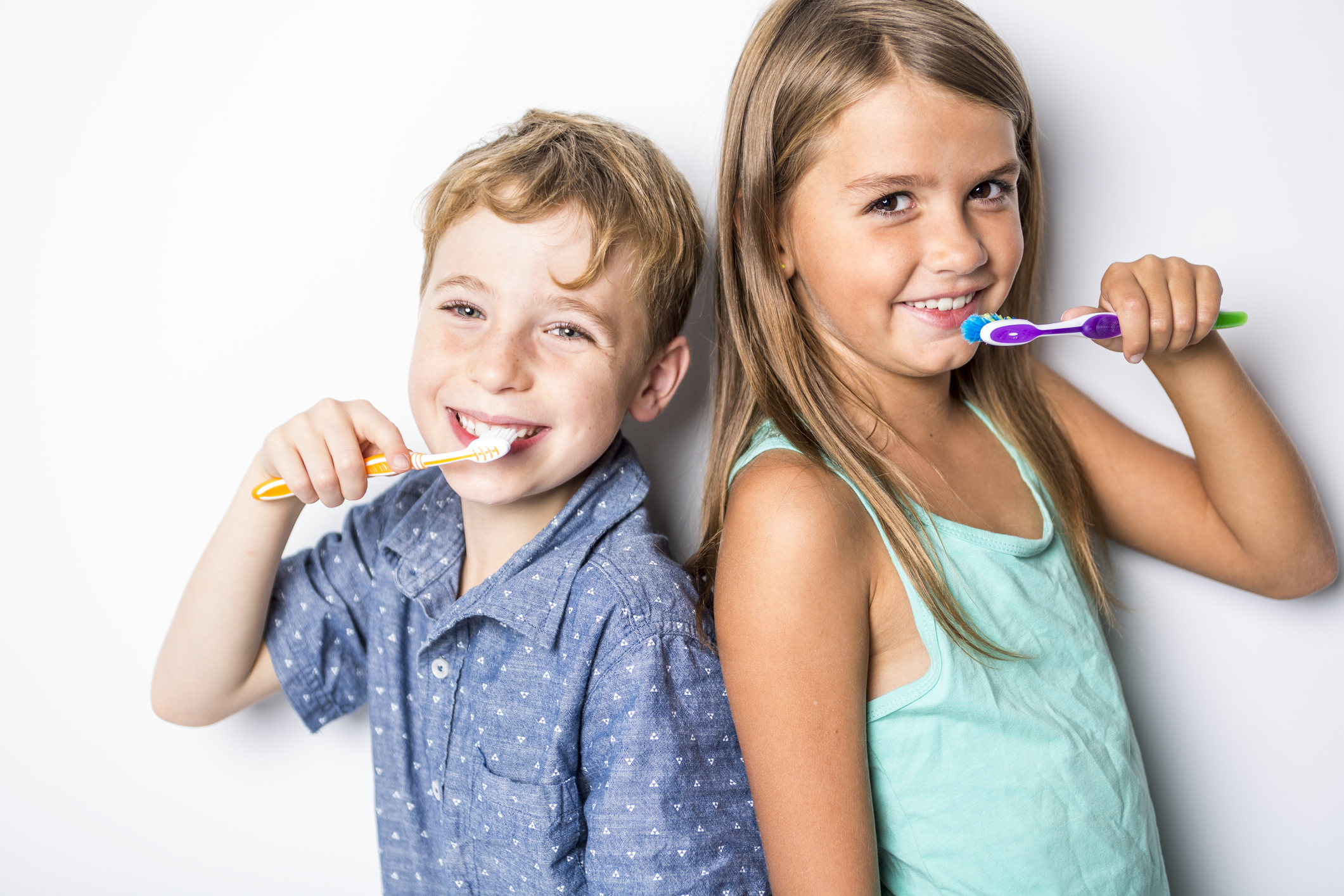 Two children perform dental care, brushing their teeth and smiling.