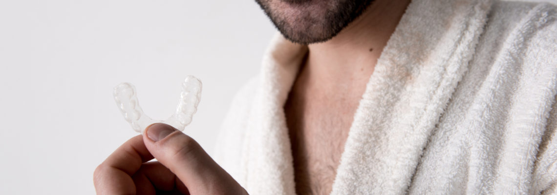 A smiling man in a bathrobe shows off the Invisalign aligner he likes better than braces.