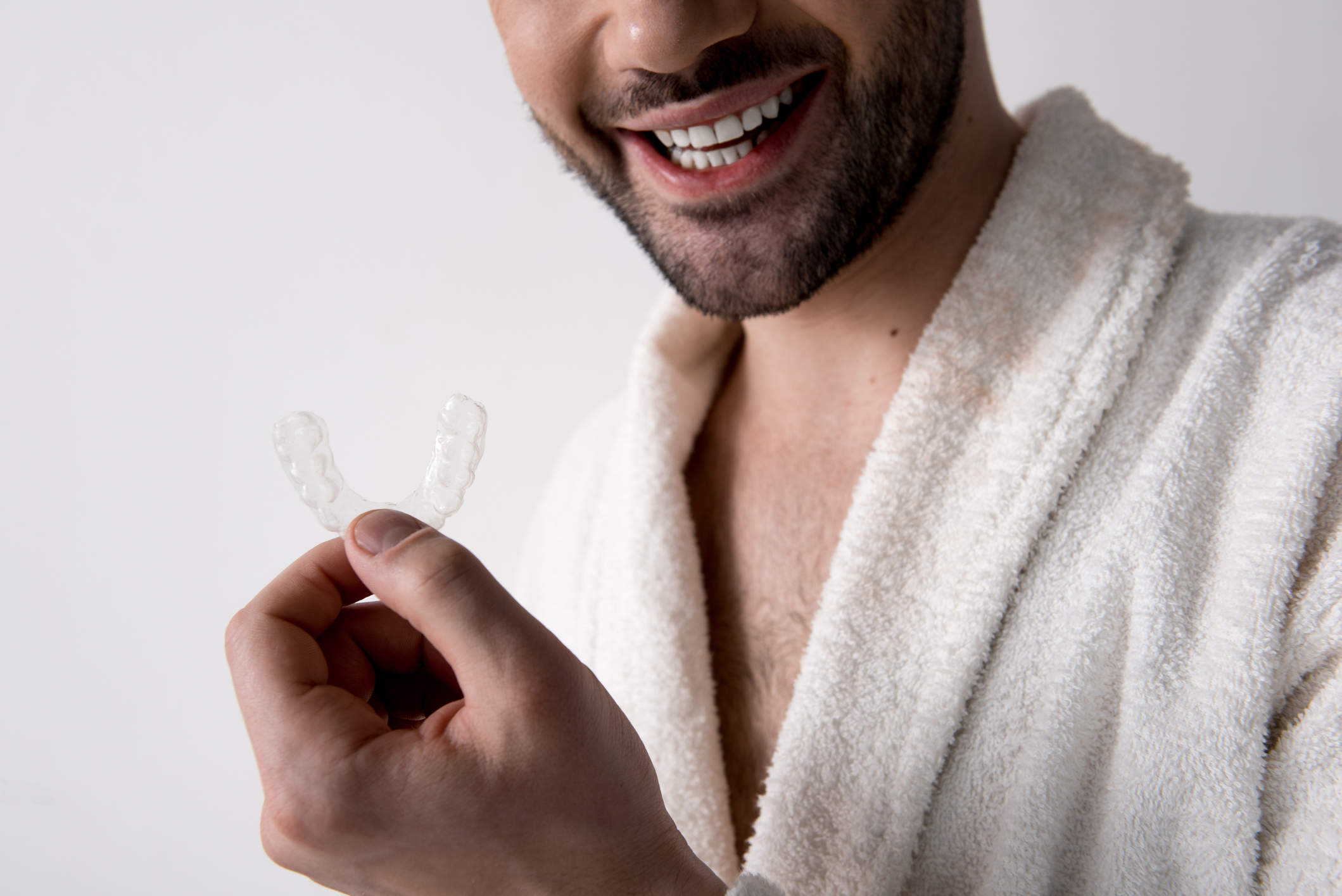 A smiling man in a bathrobe shows off the Invisalign aligner he likes better than braces.