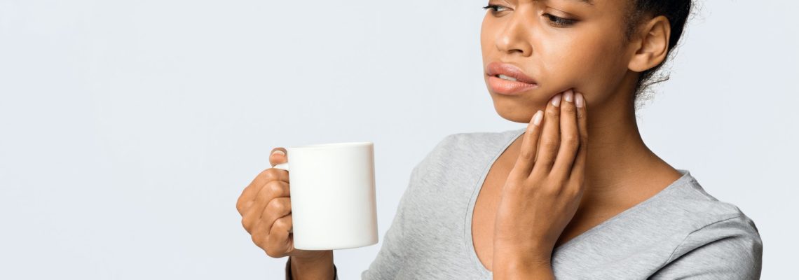 African American woman suffering from a sensitive jaw, drinking coffee