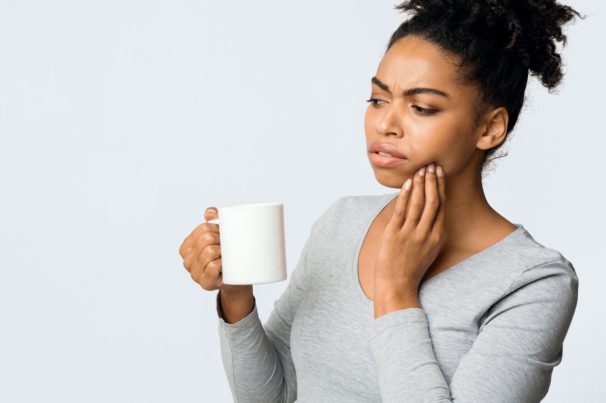 African American woman suffering from a sensitive jaw, drinking coffee