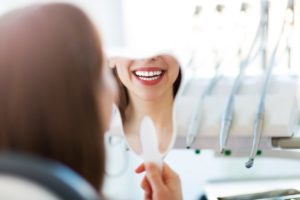 A reflection of a woman smiling into a tooth-shaped mirror shows the lower part of her face and how her smile benefits from common dental services.